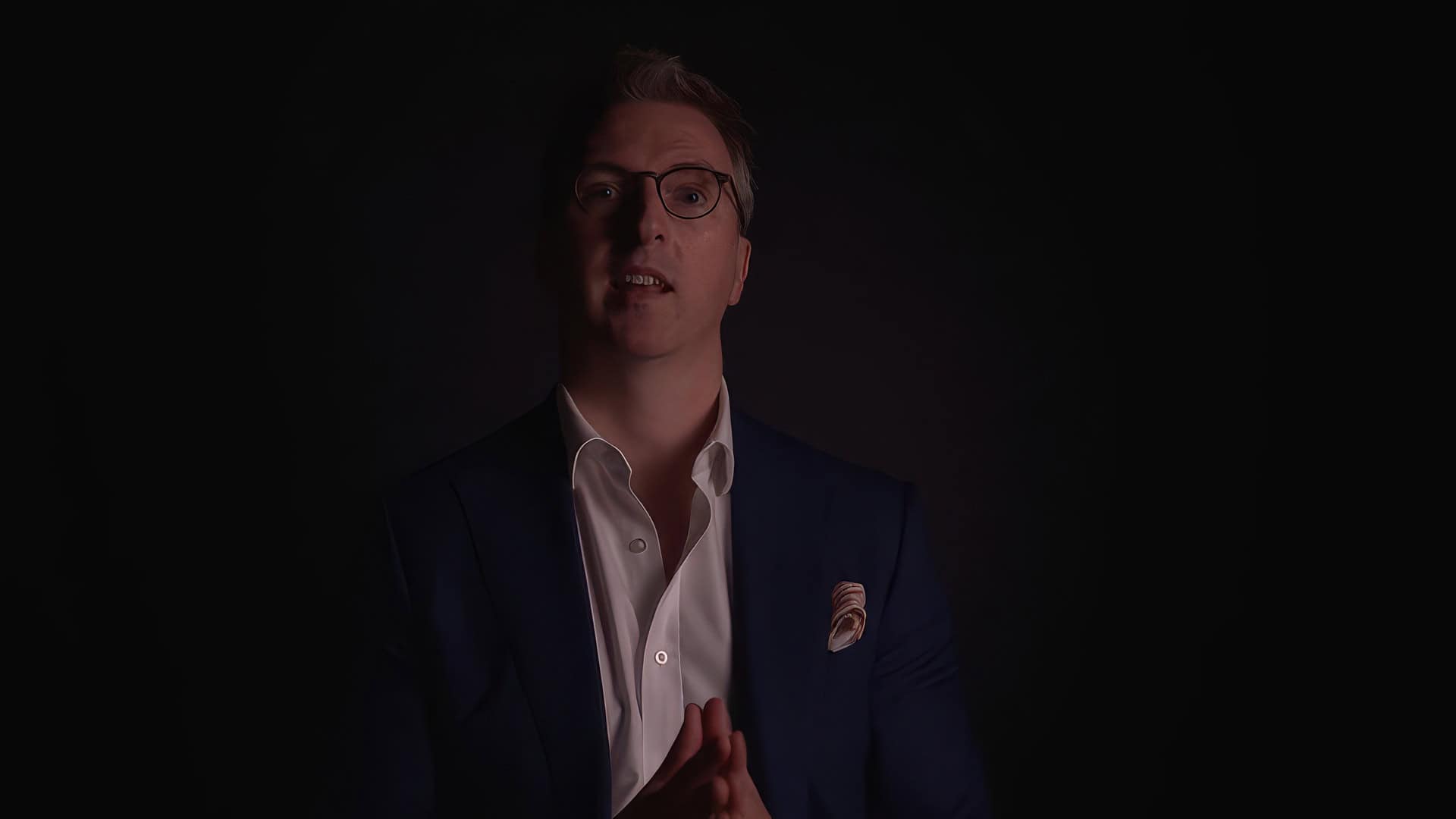 Man in suit speaking in dim lighting in soundproof studio.