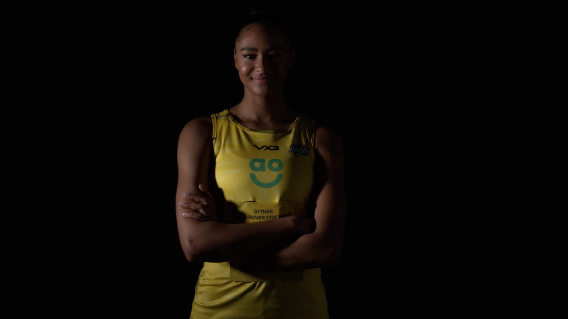 Athlete posing confidently in yellow sports uniform in blacked out studio.